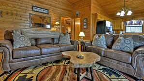 A cozy log cabin interior with a leather sofa set, a round coffee table, and a rustic wooden ceiling.