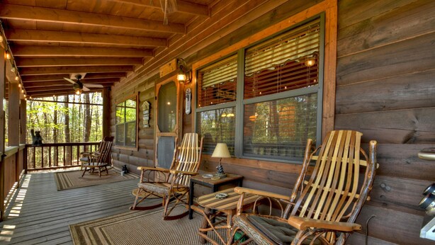 A wooden cabin with a porch, rocking chairs, and a table with a lamp.