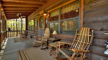 A wooden cabin with a porch, rocking chairs, and a table with a lamp.