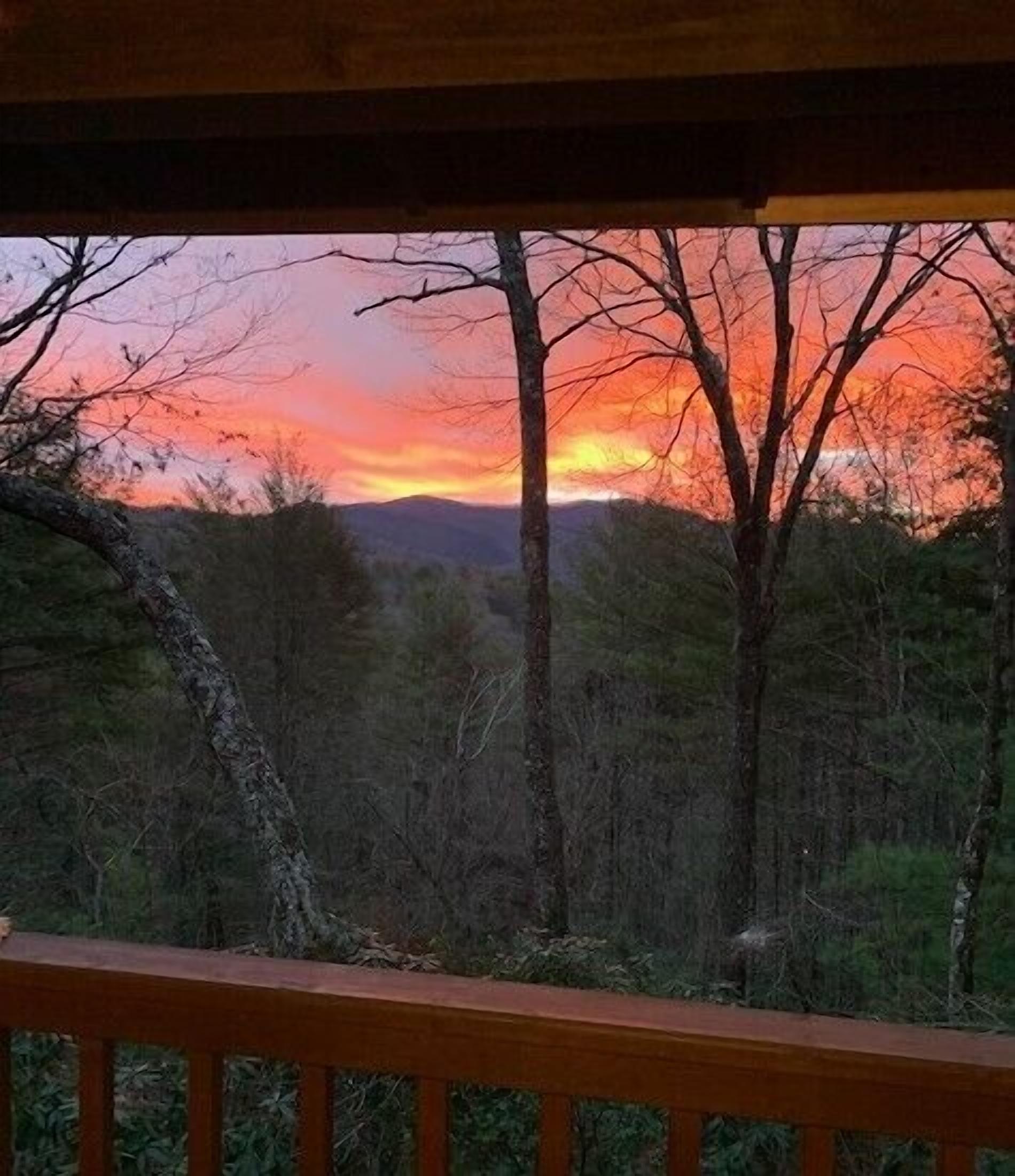 A view from a wooden balcony overlooking a forest with a sunset.