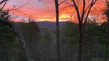 A view from a wooden balcony overlooking a forest with a sunset.