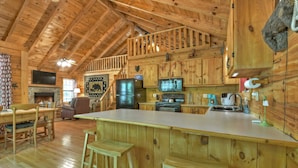 L’intérieur d’un chalet en bois comprend une cuisine, un coin repas et une cheminée.