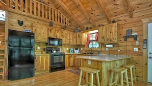 Une cuisine rustique aménagée dans une cabane en bois, comprenant un réfrigérateur, un four à micro-ondes, une cuisinière et des tabourets en bois.