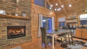 Un intérieur de chalet chaleureux avec une cheminée en pierre, des murs en bois, un coin repas et une cuisine.