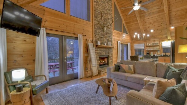 Un intérieur de chalet chaleureux avec une cheminée en pierre, des murs en bois, un canapé et un téléviseur.