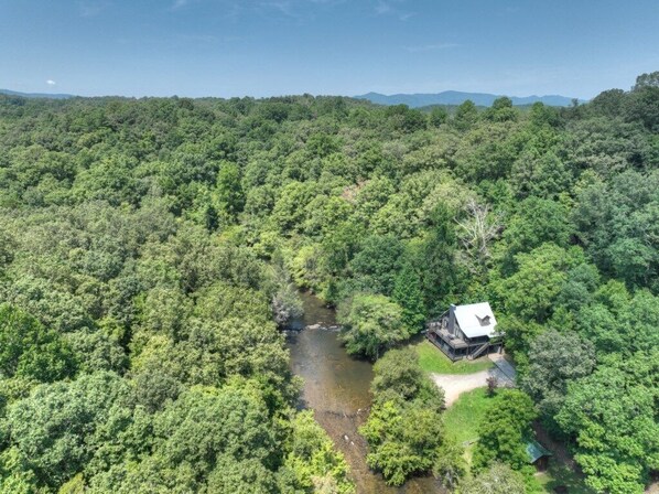 An aerial view of a forested area with a cabin by a river. - Troutlandia| Pet Friendly | Fish From Cabin | Hot Tub (McCaysville)
