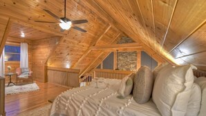 Une chambre confortable située sous les toits, avec des poutres apparentes, un plafond en pente, un lit recouvert de linge blanc, une petite table et une chaise.