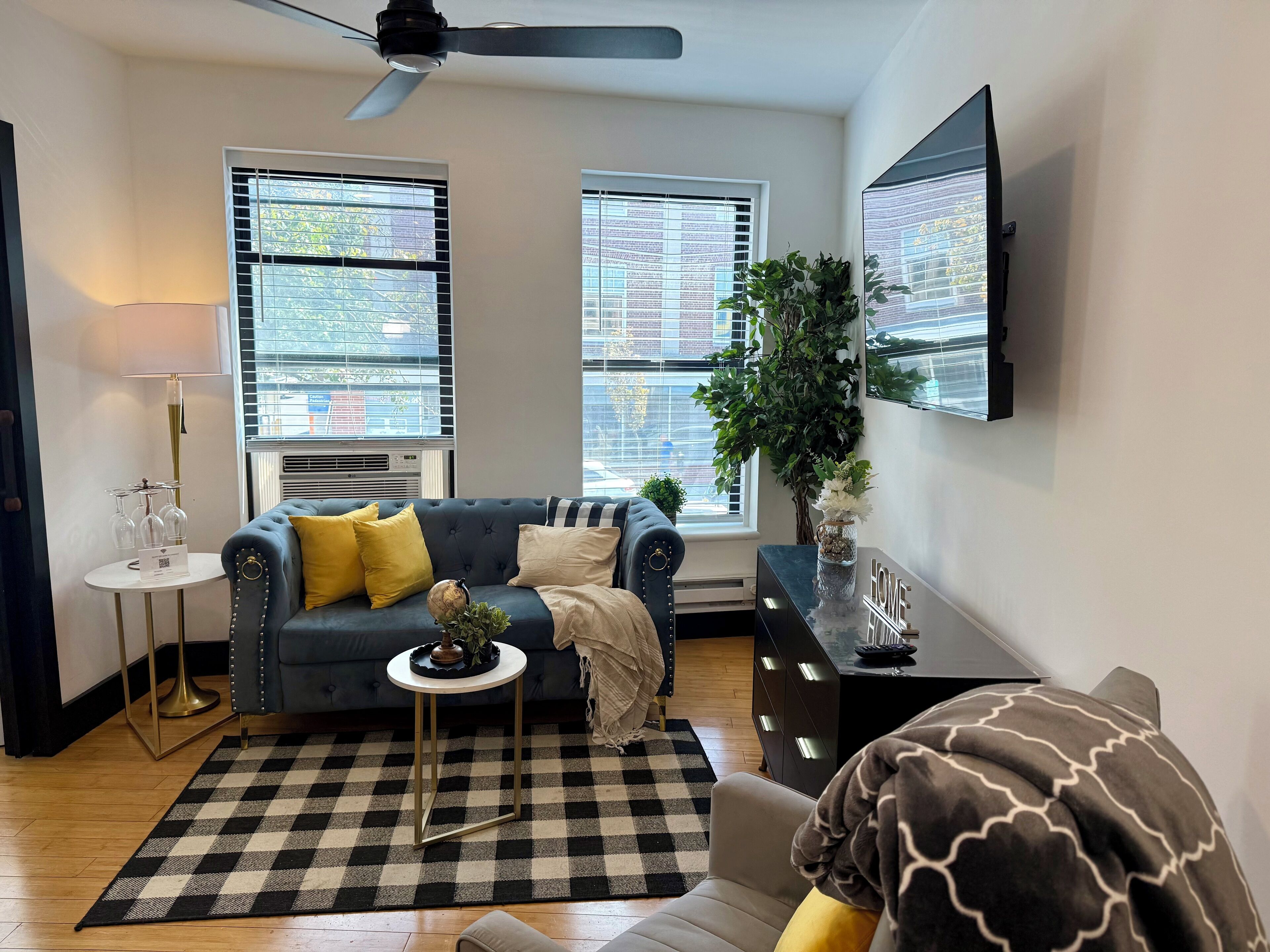 A living room with a blue sofa, yellow cushions, a checkered rug, a small round table with a globe, and a potted plant.