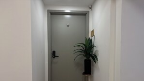 Käytävä, jossa on suljettu ovi, eteisessä oleva matto, jossa on ystävällinen teksti, ja oven vieressä oleva ruukkukasvi.