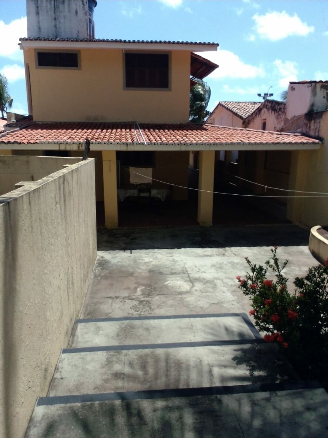 Um edifício com telhado de cerâmica, piso de concreto e uma pequena área de jardim com flores.