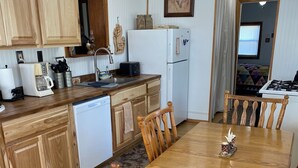 A kitchen with wooden cabinets, a dining table, and chairs. There is a refrigerator, a stove, and a sink.
