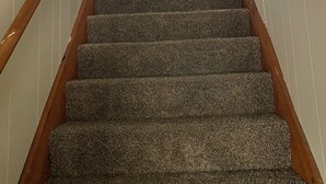 A carpeted staircase with wooden handrails, a window at the top, and framed pictures on the walls.