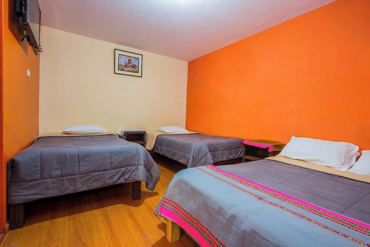 Quarto com três camas, piso de madeira e um quadro na parede.