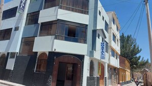 Ein mehrstöckiges Hotel mit modernem Design, das ein gut sichtbares 'HOSTAL'-Schild an der Fassade zeigt.