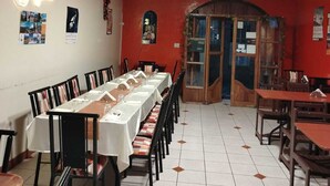 Ein Essbereich mit einem langen Tisch, gedeckt für eine Mahlzeit, Stühle und einer roten Wand mit einer Holztür.