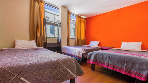 Ein Hotelzimmer mit zwei Betten, Holzboden und großen Fenstern mit Vorhängen.