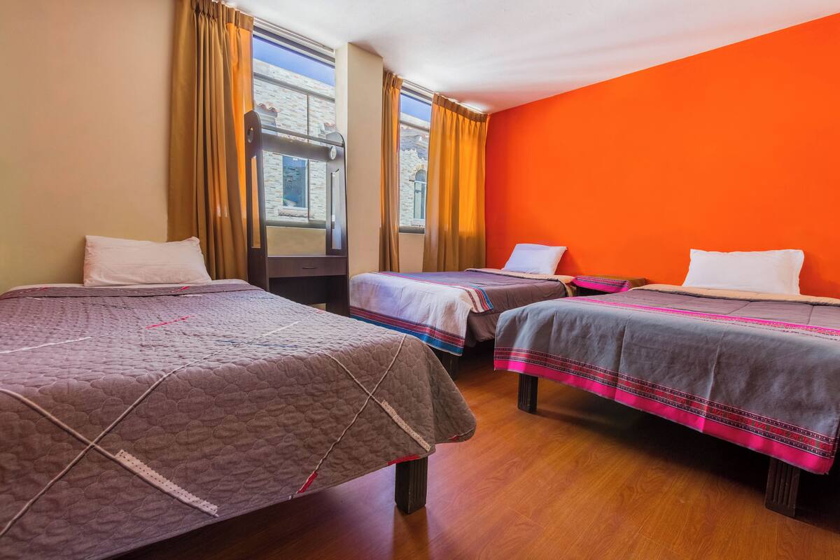 Quarto de hotel com duas camas, soalho em madeira e janelas amplas com cortinas.