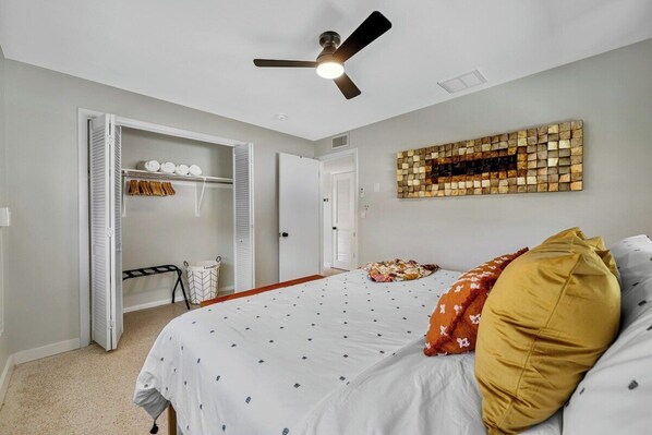A bedroom with a bed, a ceiling fan, a wall art piece, and a walk-in closet with hanging clothes.