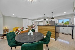 A modern kitchen with white cabinets, a black countertop, and a dining area with a marble table and green chairs. - Hot Tub | Private Home | Ping Pong | Mins to Beach (Largo)