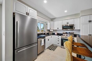 A modern kitchen with stainless steel appliances, white cabinetry, and a black and white patterned rug. - Hot Tub | Private Home | Ping Pong | Mins to Beach (Largo)