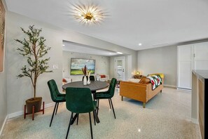 A modern living room with a sofa, a dining area with chairs, a potted plant, and a ceiling light fixture.