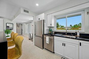A modern kitchen with white cabinets, stainless steel appliances, and a window with a view of greenery.