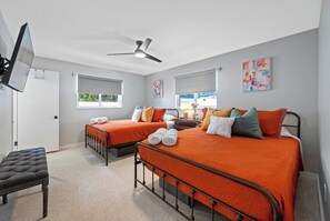 Une chambre d’hôtel avec deux lits simples, un banc, un ventilateur de plafond et des œuvres d’art accrochées aux murs.