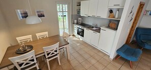 Una cocina compacta con armarios blancos, una mesa de comedor con sillas y una silla azul.