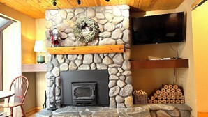 A stone fireplace with a television above it, a wooden ceiling, and a chair to the left. - Mountain Retreat near mt Baker, cozy 1bedroom Condo w/ Pool, Hot Tub, Crib, wifi (Deming)