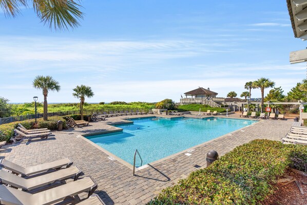 A rectangular swimming pool with lounge chairs and a covered pavilion in the background.