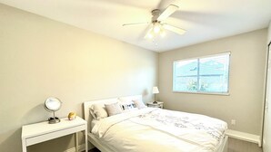 Ein Schlafzimmer mit einem Bett, einem Nachttisch mit Lampe, einem Deckenventilator und einem Fenster mit Jalousien.