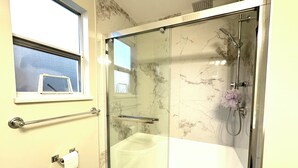 Ein modernes Badezimmer mit einer gläsernen Duschkabine, einer weißen Badewanne und einem Fenster über der Toilette.