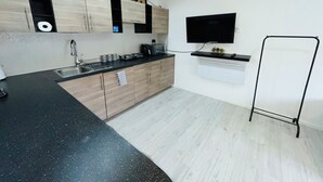 A modern kitchen with a black countertop, wooden cabinets, a built-in oven, and a black TV mounted on the wall.