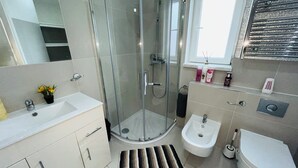 A modern bathroom with a glass shower enclosure, a bidet, a toilet, and a sink.