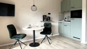 A modern kitchen with a dining area, featuring a round table, two chairs, a hanging light fixture, and light-colored cabinets.