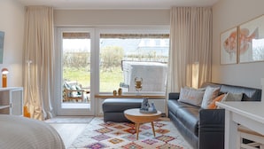 Ein gemütliches Zimmer mit einer Couch, einem kleinen Tisch und Blick ins Freie durch große Fenster.