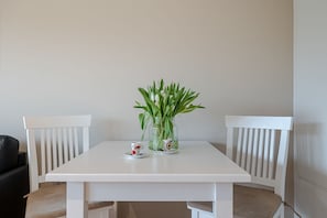 Uma mesa branca com duas cadeiras, um vaso de vidro com plantas verdes e duas chávenas com pires.