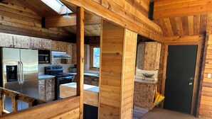 A wooden cabin interior with a kitchen area, a dining space, and a door. - Hideout in the Mountains HOT TUB and River access (Gallatin Gateway)