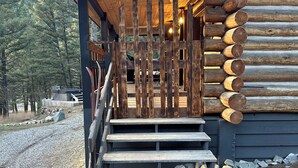 A wooden cabin with a staircase leading to a porch, surrounded by a gravel path and trees. - Hideout in the Mountains HOT TUB and River access (Gallatin Gateway)