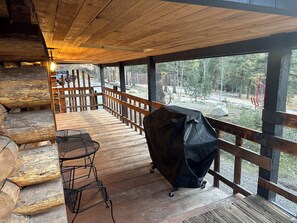 Eine überdachte Terrasse im Freien mit Holzmöbeln, einem Grill und Blick auf eine bewaldete Landschaft.