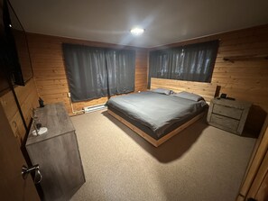 Ein Schlafzimmer mit einem Bett mit Holz-Kopfteil, einem kleinen Nachttisch, einem Beistelltisch und einer fest installierten Heizung.
