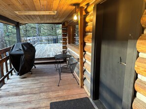 Eine Holzterrasse mit Grill, Tisch und Stühlen.