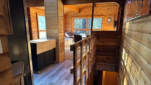 A wooden cabin interior with a kitchen area, a dining space, and a staircase. - Hideout in the Mountains HOT TUB and River access (Gallatin Gateway)