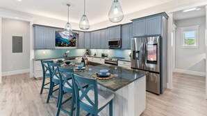 Una cucina moderna con armadietti blu, una grande isola con sgabelli da bar, elettrodomestici in acciaio inossidabile e luci a sospensione.