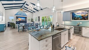 Un'ampia cucina con isola centrale, lampade a sospensione moderne e zona pranzo con sedie blu.