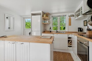 Eine moderne Küche mit weißen Schränken, einer Holz Arbeitsplatte und einem Fenster mit Blick auf Grünflächen.