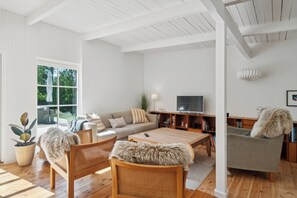 Ein modernes Wohnzimmer mit einer Couch, Sesseln, einem Couchtisch, einem Fernseher und einem Bücherregal.