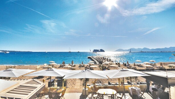 Un restaurant situé en bord de mer, avec une terrasse et des parasols, offrant une vue sur la mer et un navire au loin.