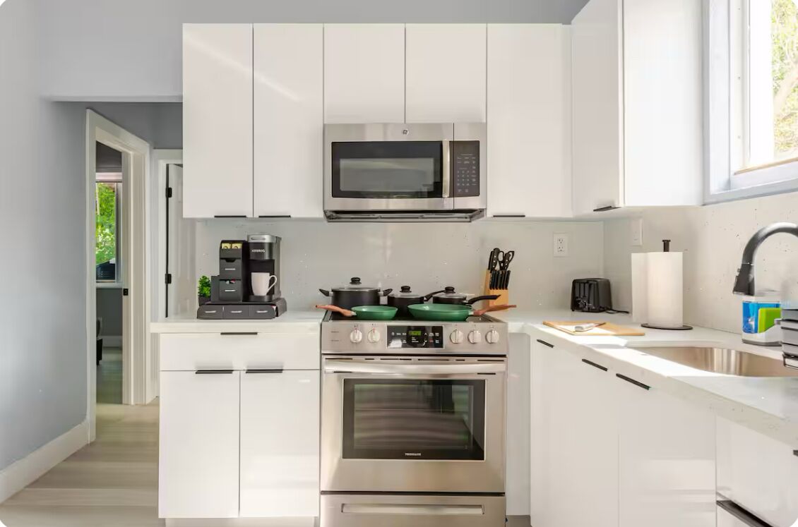Une cuisine moderne avec des meubles blancs, un four à micro-ondes encastré, une cuisinière et un four.