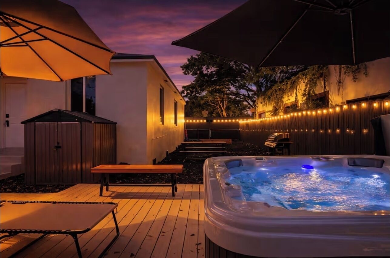 Uma banheira de hidromassagem com luz azul, deck de madeira, área de estar externa e luzes de cordão.